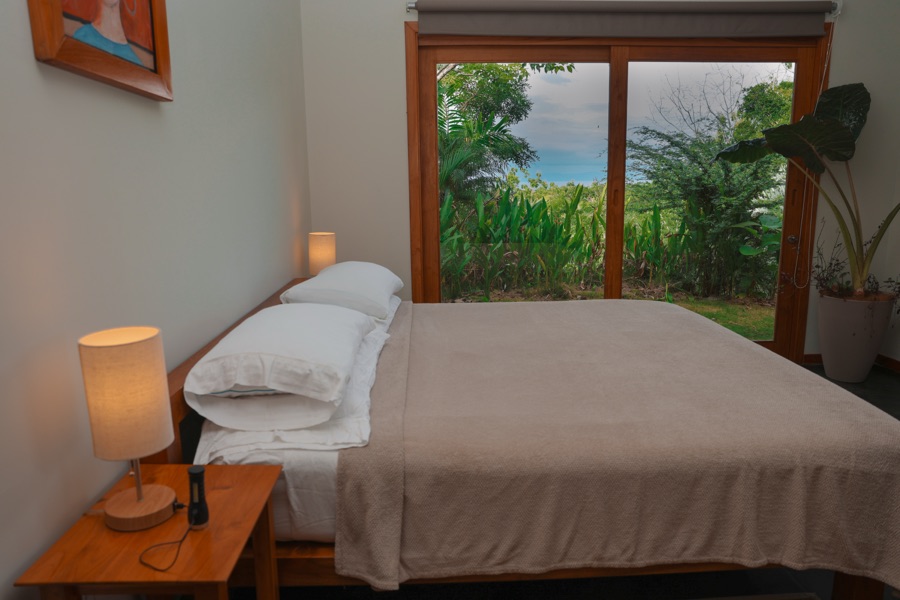 Bed beside a glass slider with garden views in the Oceanview Studio